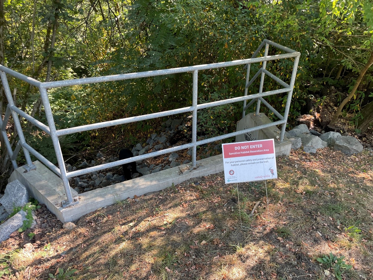 Sign which reads "Do Not Enter" in front of a metal railing amongst shrubbery. 
