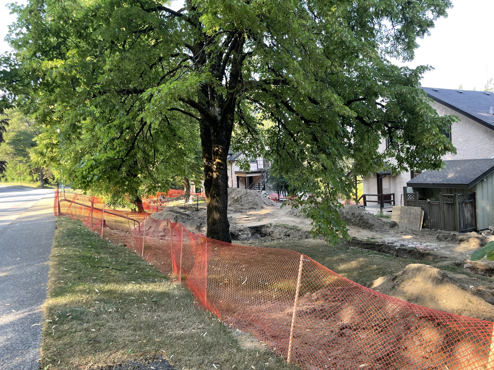 piles of dirt from a dug up trench that is surrounded by a temporary plastic orange fencing