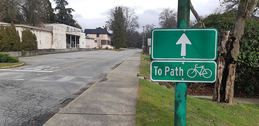 A green sign with white arrow pointing to the new Designated Cycling Route next to a road