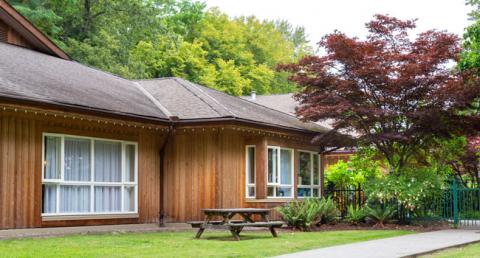 Lodge with windows beside a lawn, trees and a bench